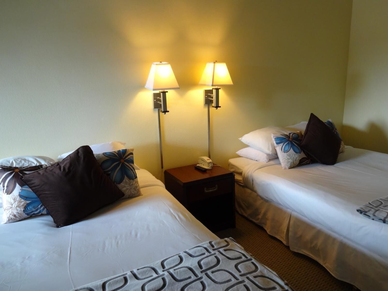 A hotel room with two beds, each with a pillow and a bedside table with a lamp.