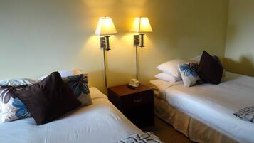 A hotel room with two beds, each with a pillow and a bedside table with a lamp.