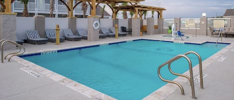 A swimming pool with lounge chairs and a covered seating area.