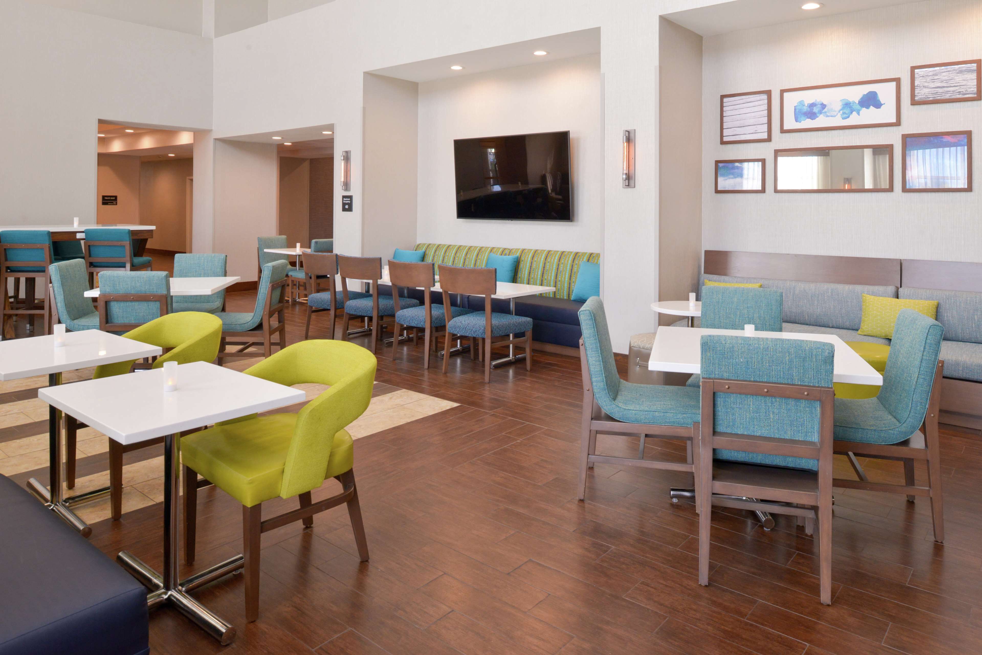 A modern dining area with multiple seating options including booths and tables, a flat-screen TV mounted on the wall, and framed artwork on the walls.