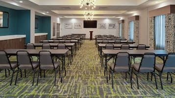 A conference room with multiple tables and chairs, a carpeted floor, and a large chandelier.
