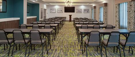A conference room with multiple tables and chairs, a carpeted floor, and a large chandelier.