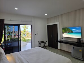 A hotel room with a bed, a TV on the wall, a minibar, and a sliding glass door leading to a balcony with a view of a beach. - Samui Pier Beach Front Resort (Koh Samui)