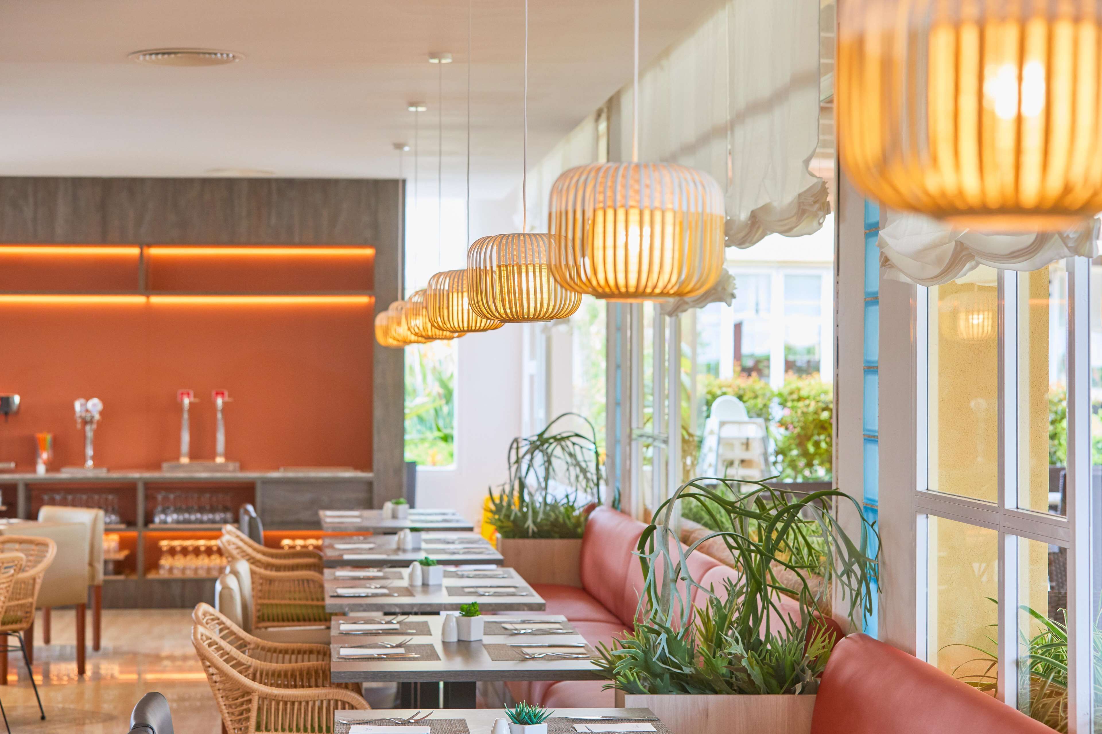 A restaurant with a long dining table, cushioned seating, and hanging pendant lights.