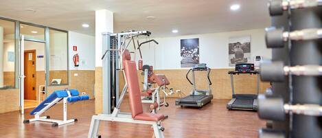 Ein Fitnessraum mit verschiedenen Trainingsgeräten, darunter ein Laufband, ein Rudergerät und eine Hantelbank.