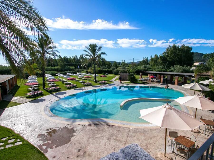 Una piscina con zonas de descanso alrededor, palmeras y cielo despejado.