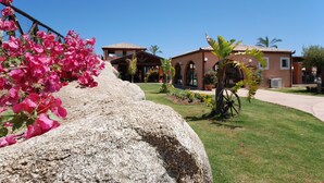 A building with a patio area, a stone wall, and a garden with pink flowers.
