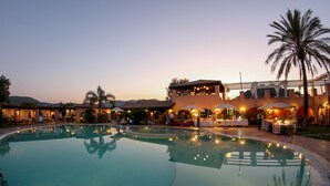 A swimming pool with a patio area, palm trees, and a building with outdoor seating.