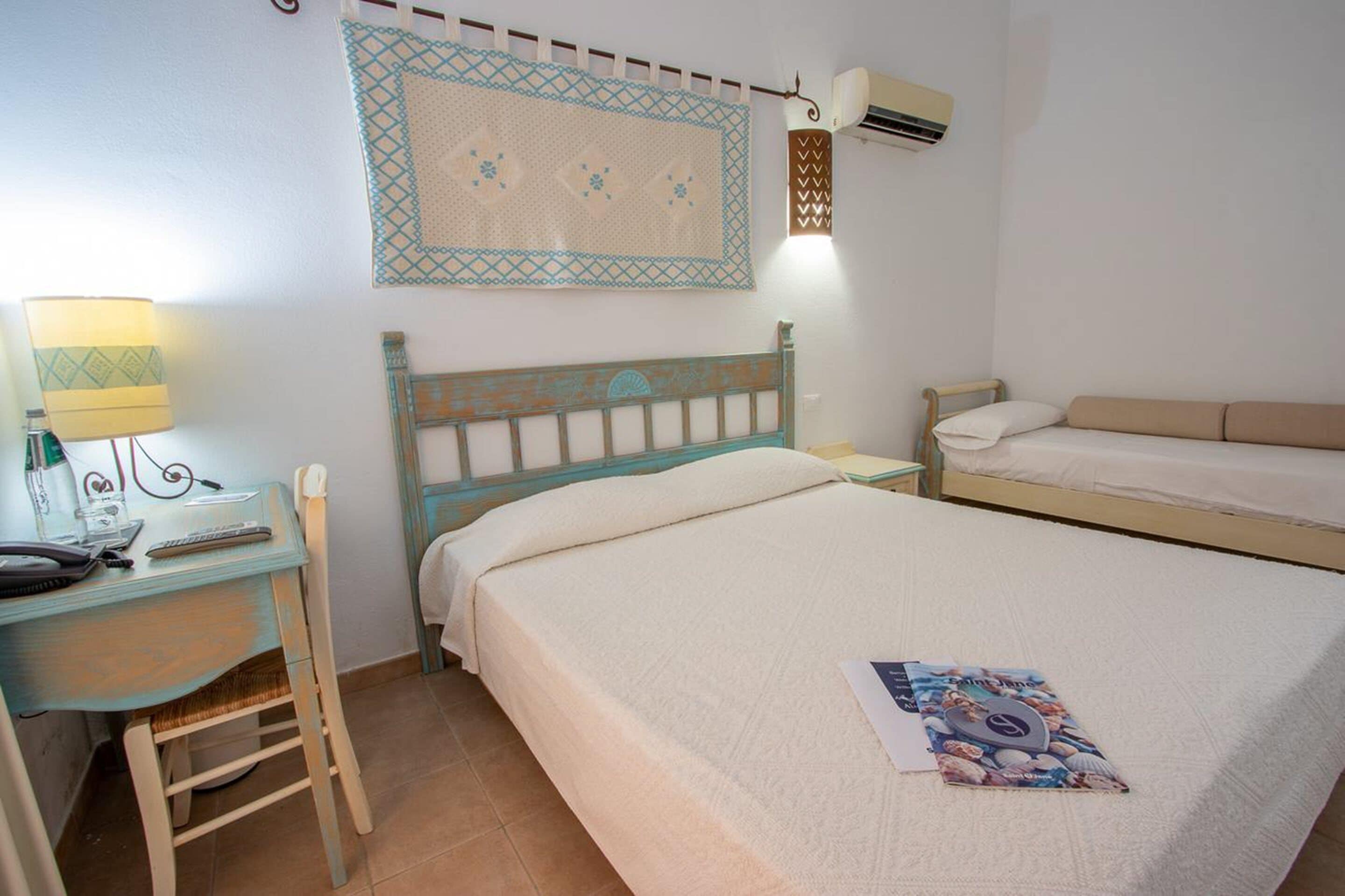 A bedroom with a bed, a desk with a lamp, and a wall-mounted air conditioner.