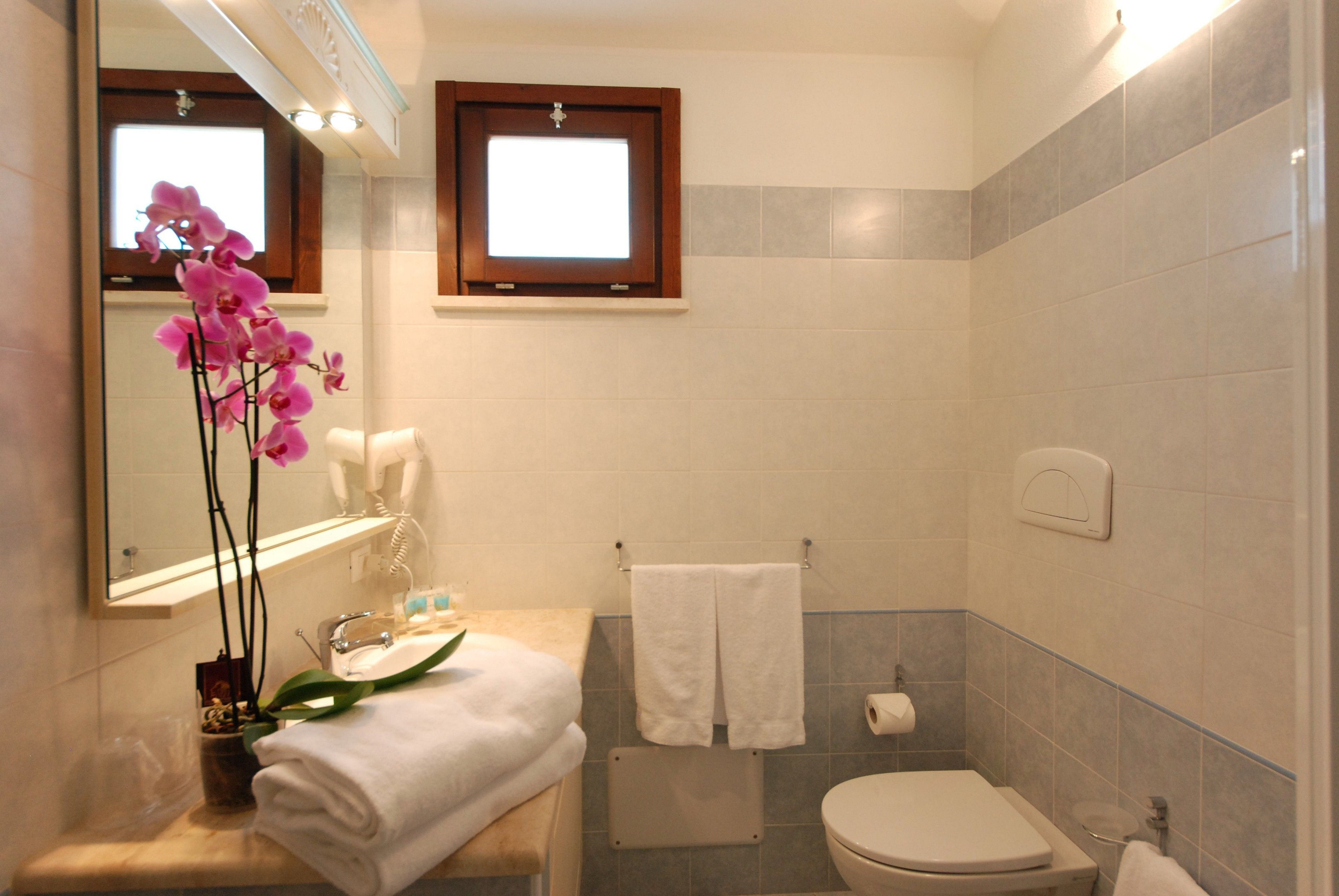 A bathroom with a sink, mirror, toilet, and a window.
