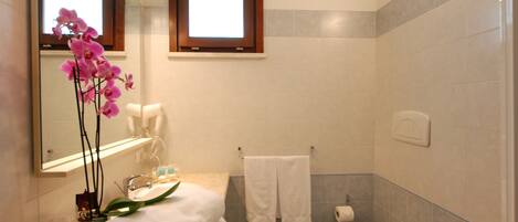 A bathroom with a sink, mirror, toilet, and a window.