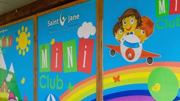 Une fresque murale colorée pour le club Saint Jane Mini, représentant un soleil, des nuages, un arc-en-ciel et une fusée.