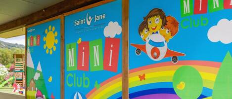 Um mural colorido para o Saint Jane Mini Club, com sol, nuvens, um arco-íris e um foguete.