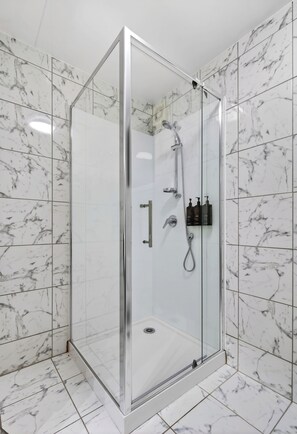 Cabina de ducha con paredes de vidrio, cabezal de ducha manual y rociador de mano.