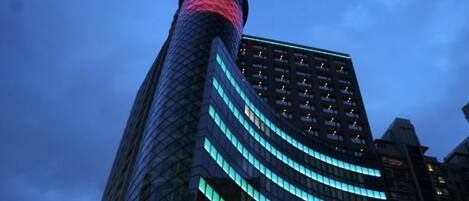A modern building with a curved glass facade and a prominent cylindrical structure at the top.