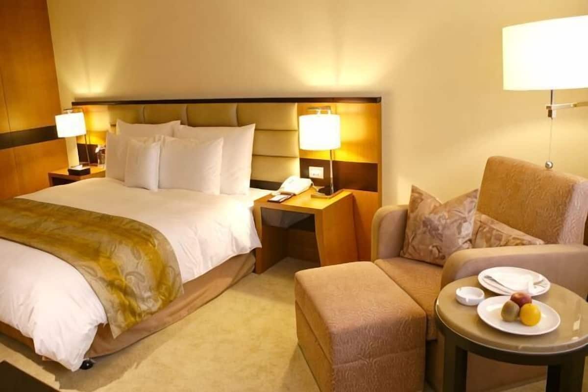 A hotel room with a large bed, bedside tables with lamps, a sofa, and a small table with a plate of fruit.
