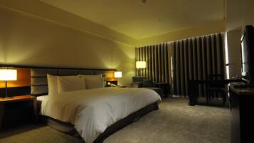 A hotel room with a large bed, two bedside tables with lamps, a desk with a chair, and a TV.