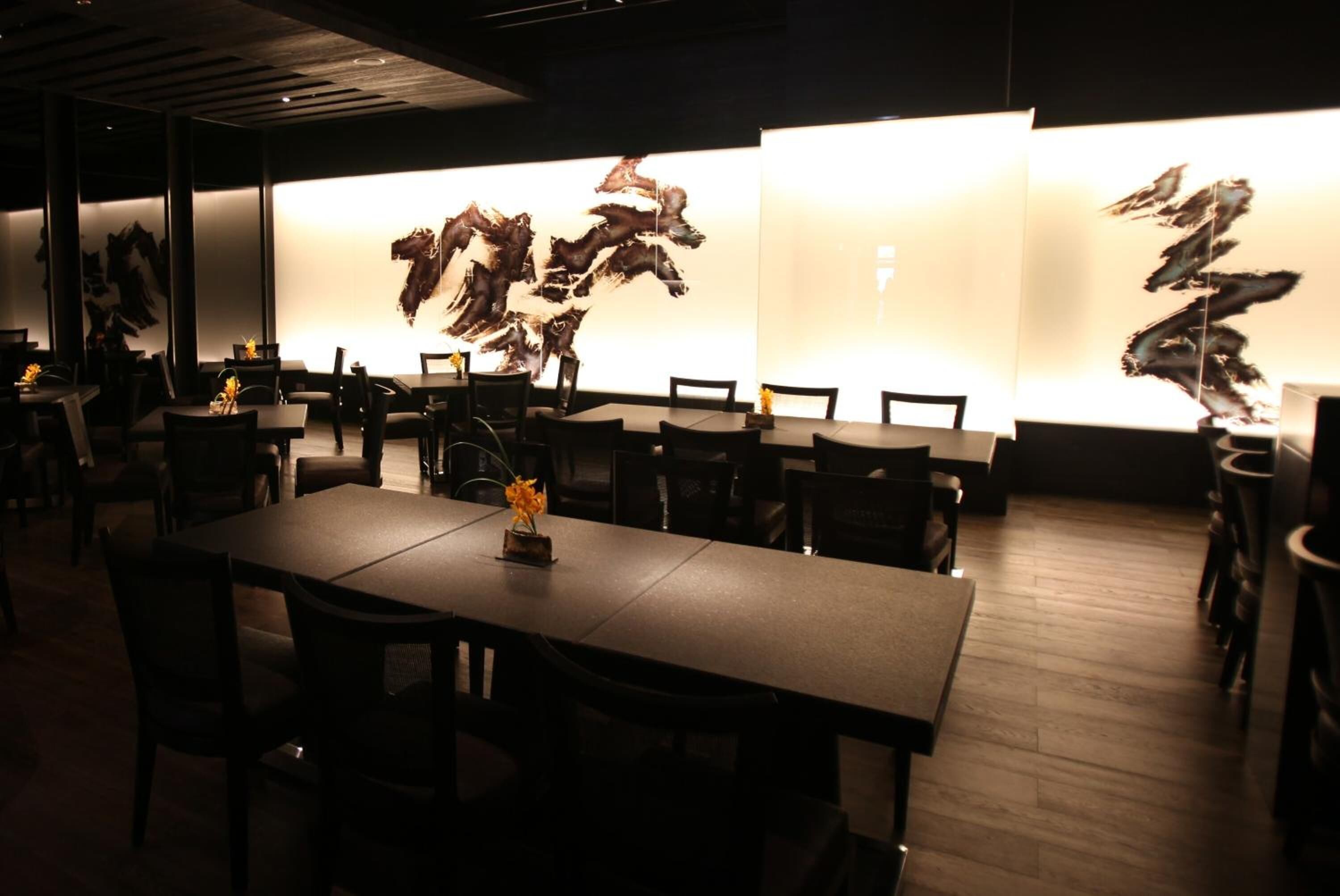 Un restaurant doté de nombreuses tables et chaises, agrémenté d’œuvres d’art murales abstraites et offrant une ambiance chaleureuse et tamisée.