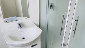 A modern bathroom with a white sink, mirror, and glass shower enclosure. - Alpha Motor Inn (Palmerston North)