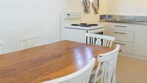 A small kitchen with white cabinets, a stove, and a wooden dining table with chairs. - Alpha Motor Inn (Palmerston North)