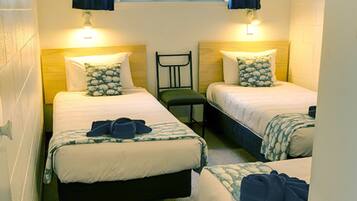 Quarto com duas camas, cada uma com travesseiro e cabeceira. Há uma cadeira no centro do quarto.