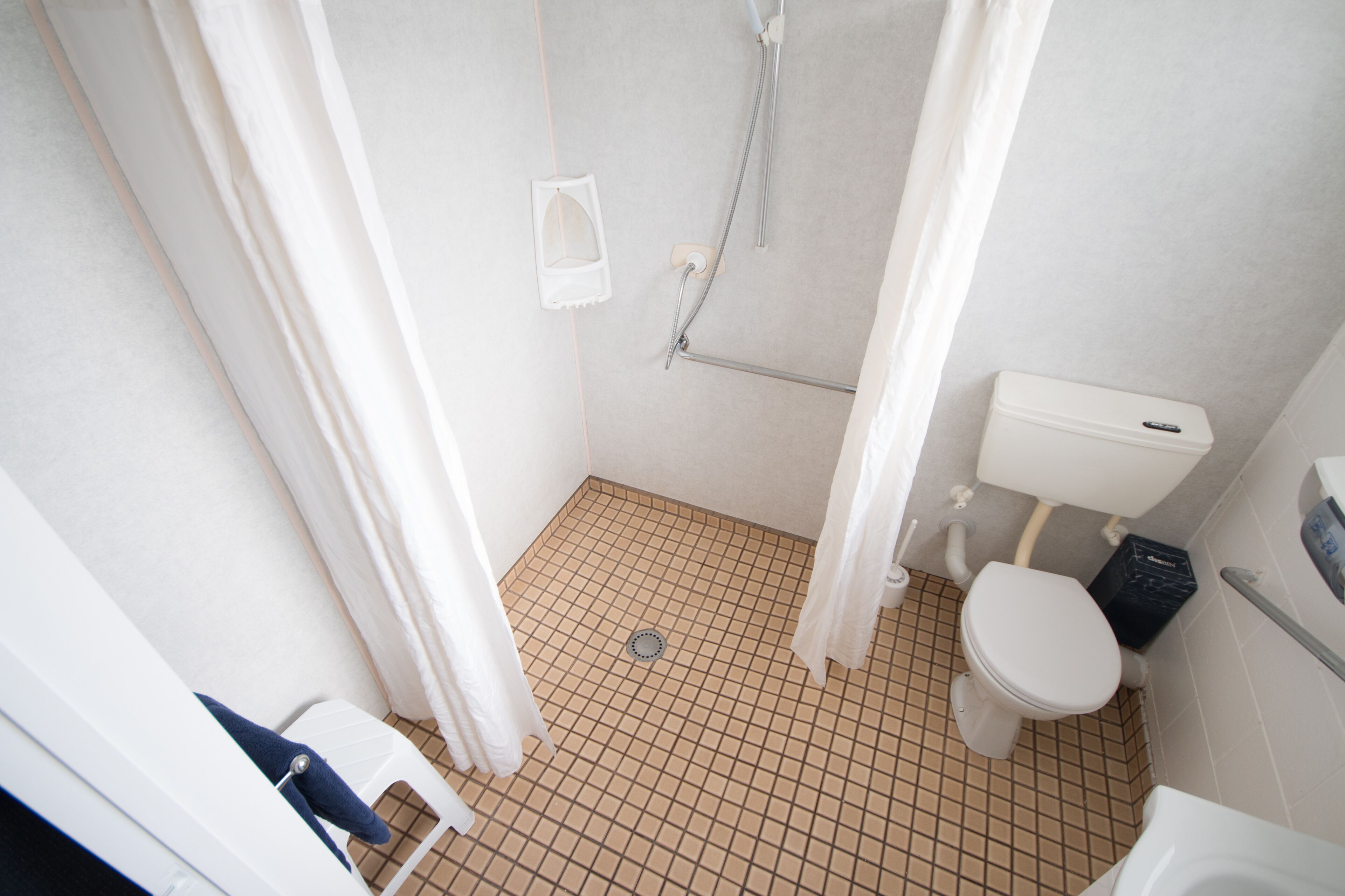 Un baño pequeño con azulejos, que incluye un inodoro, ducha y un lavamanos blanco.