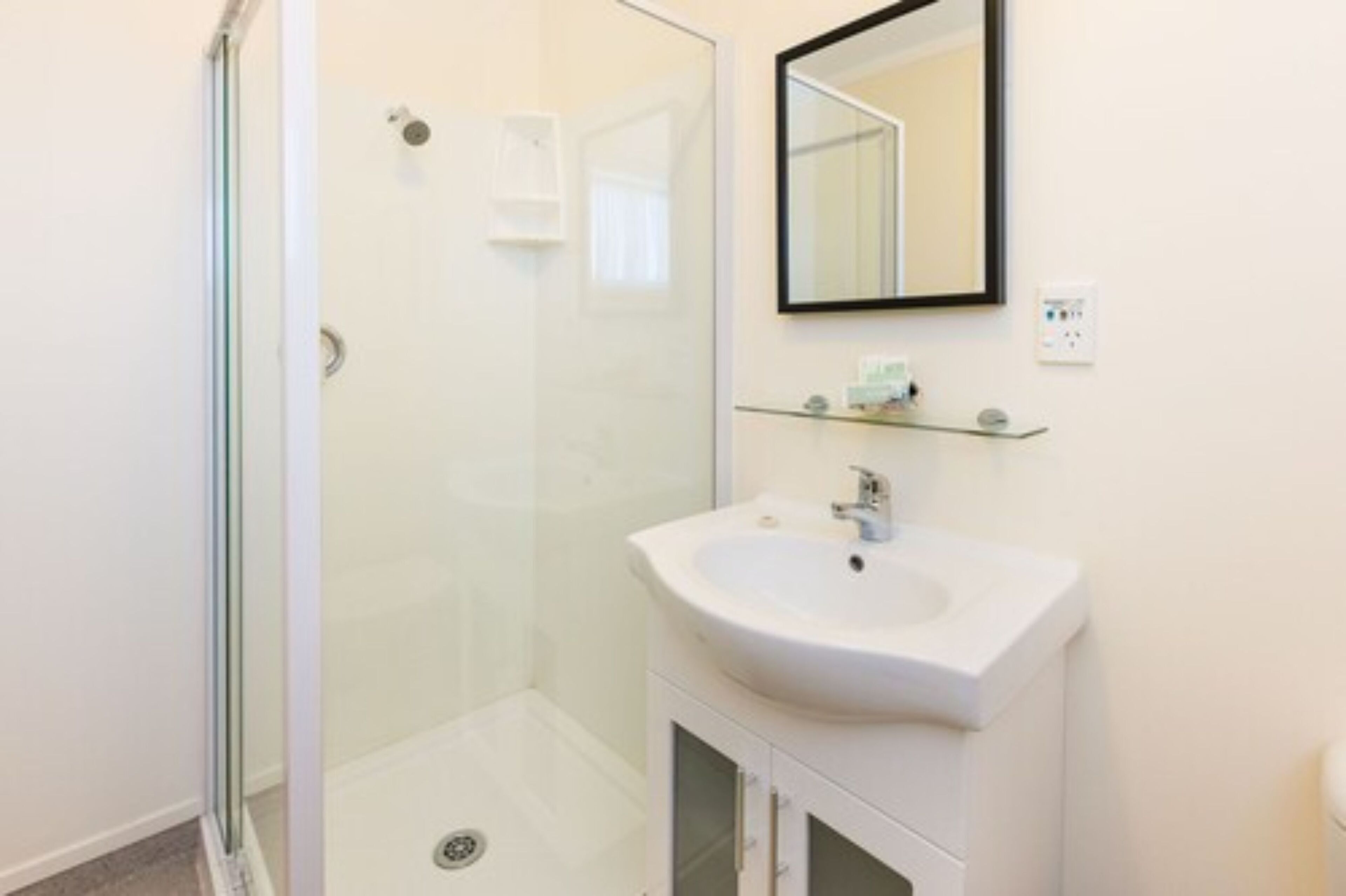 A bathroom with a glass-enclosed shower, a white sink, and a mirror above it.