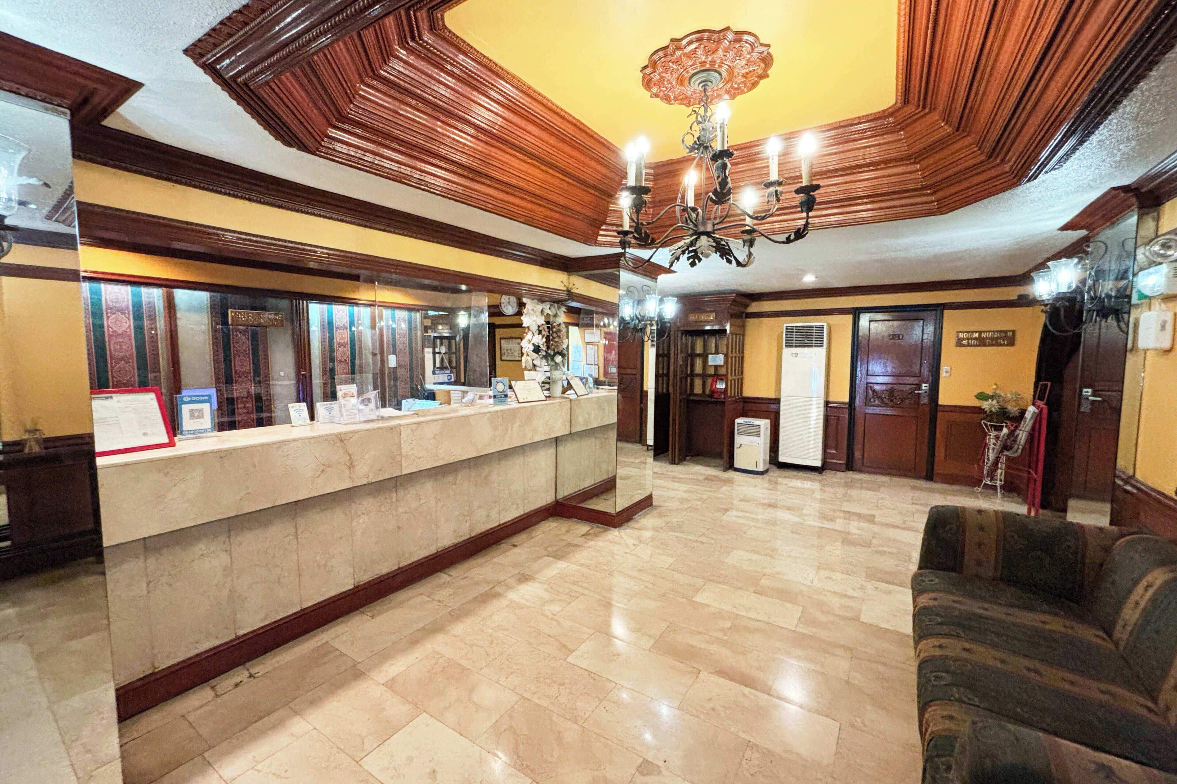 A hotel lobby with a reception desk, a chandelier, a sofa, and a clock on the wall.