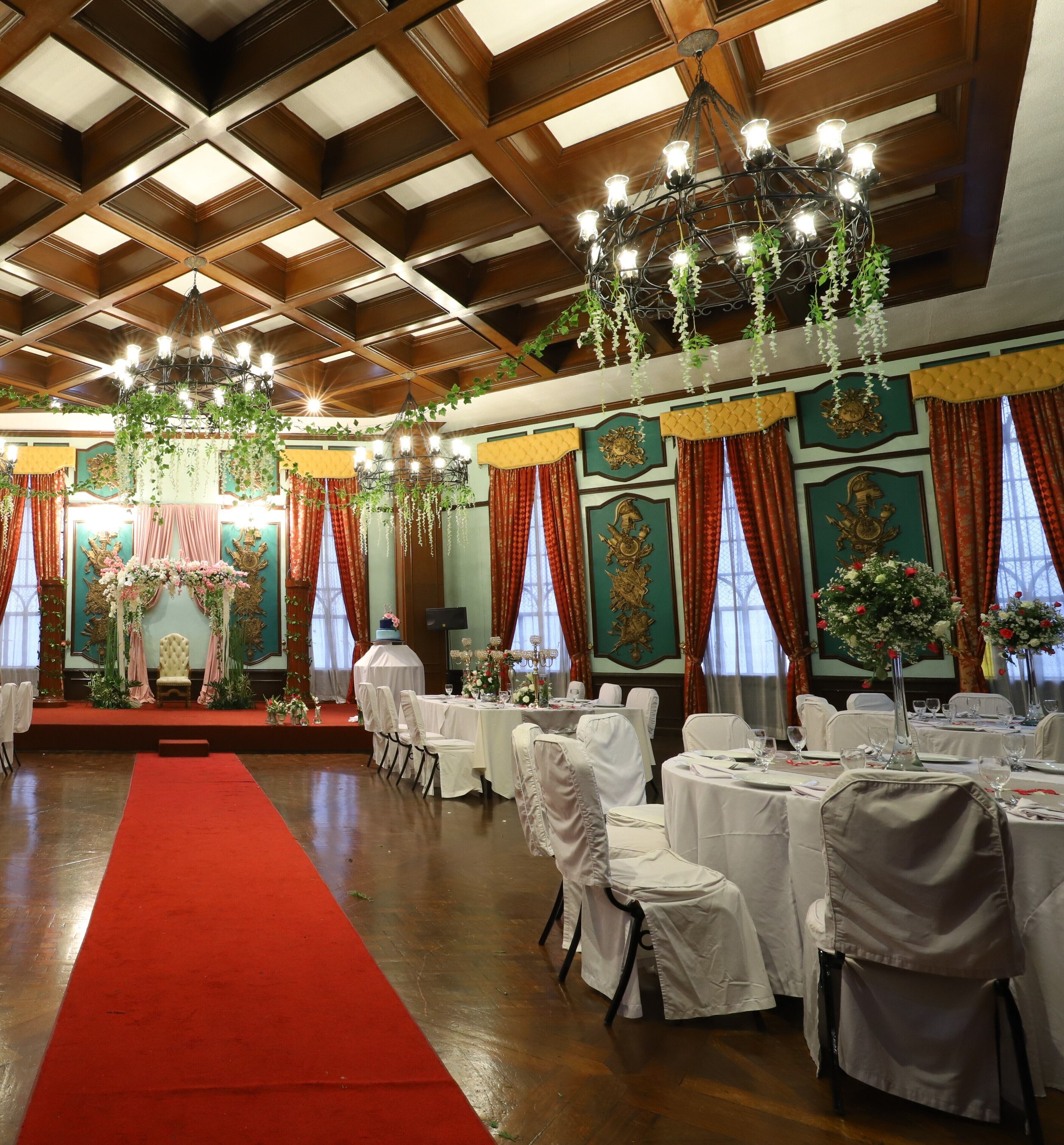 Une salle de banquet avec un tapis rouge, des nappes blanches et des chaises.