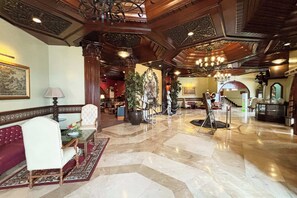 A grand lobby with a marble floor, ornate wooden ceiling, and a chandelier. There are seating areas with a red sofa and a white chair. - Camelot Hotel Quezon City powered by Cocotel (Quezon City)