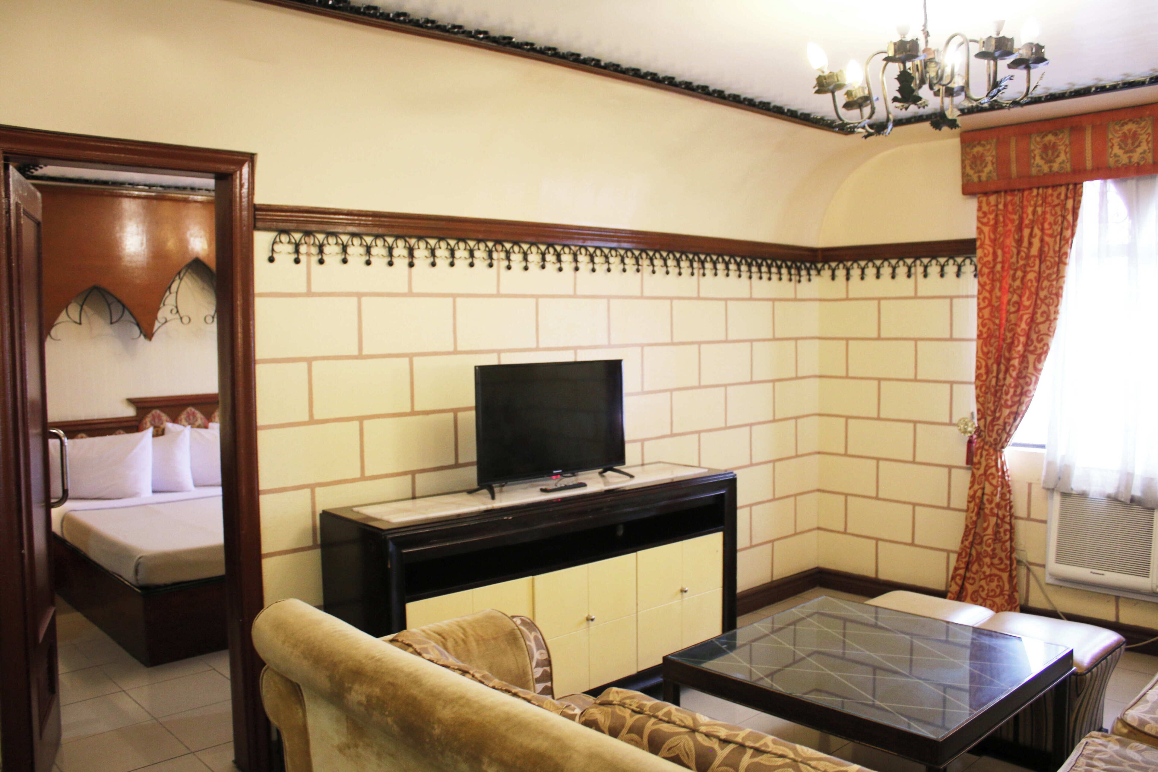 A hotel room with a bed, a television on a stand, a sofa, a coffee table, and a decorative wall.