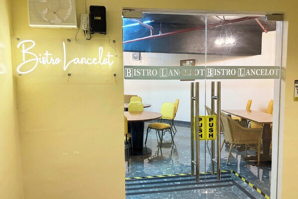 A restaurant interior with a neon sign reading "Bistro Lancelot," tables with yellow chairs, and a glass door with a push sign. - Camelot Hotel Quezon City powered by Cocotel (Quezon City)