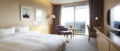 Habitación de hotel con una cama grande, un escritorio, una silla, un televisor y un balcón con vistas.