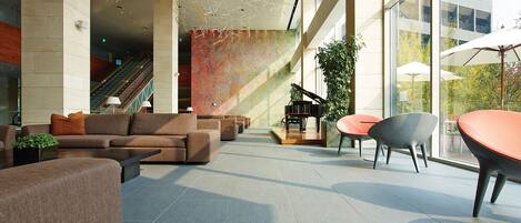 A spacious lobby with a grand piano, comfortable seating, and large windows offering views of the outdoors.