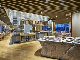 Un restaurante moderno con un buffet central, suelo de madera y grandes ventanales con vistas al exterior.