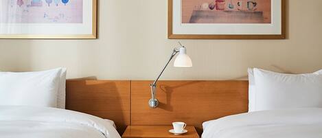 A hotel room with two beds, a nightstand with a lamp, and two framed artworks on the wall.