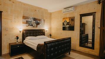 A bedroom with a large bed, a nightstand, a wall-mounted air conditioner, and a mirror.
