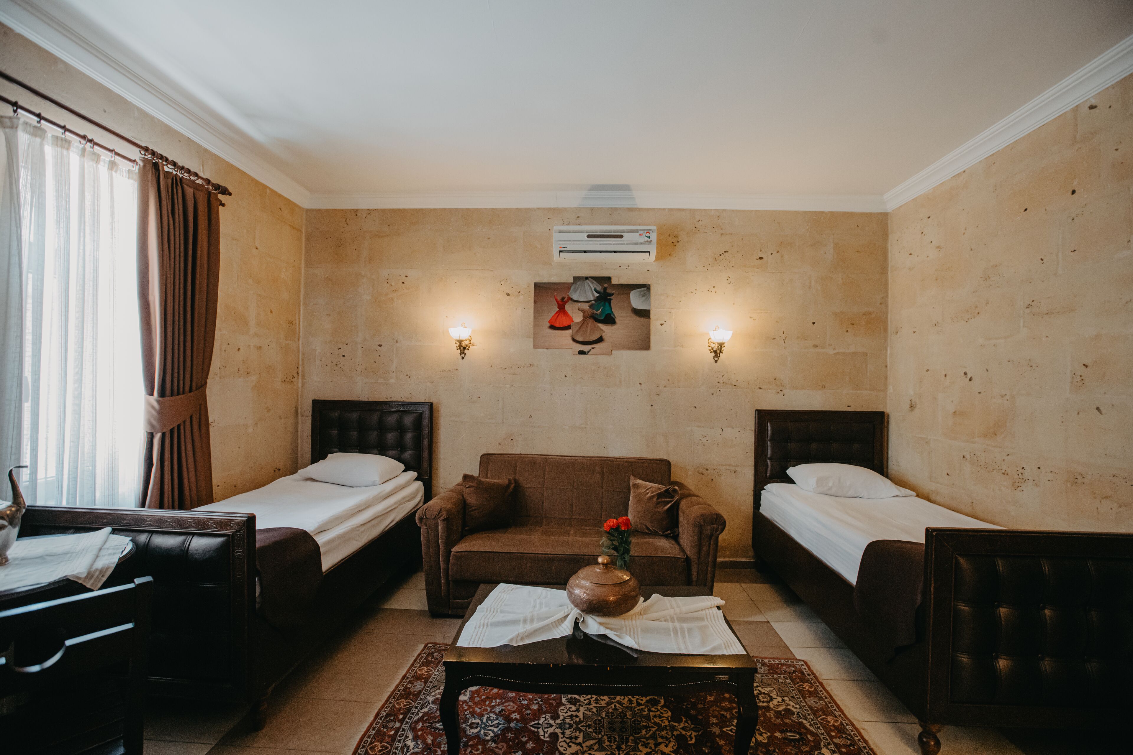 Una habitación de hotel con dos camas individuales, un sofá, una mesita y un jarrón decorativo.