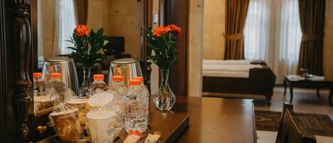 A hotel room with a dining table set with coffee cups, bottled water, and snacks. There are two vases with flowers on the table.