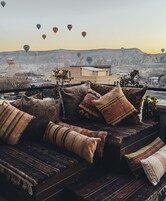 Un rincón acogedor con cojines estampados y vistas a globos aerostáticos a lo lejos.