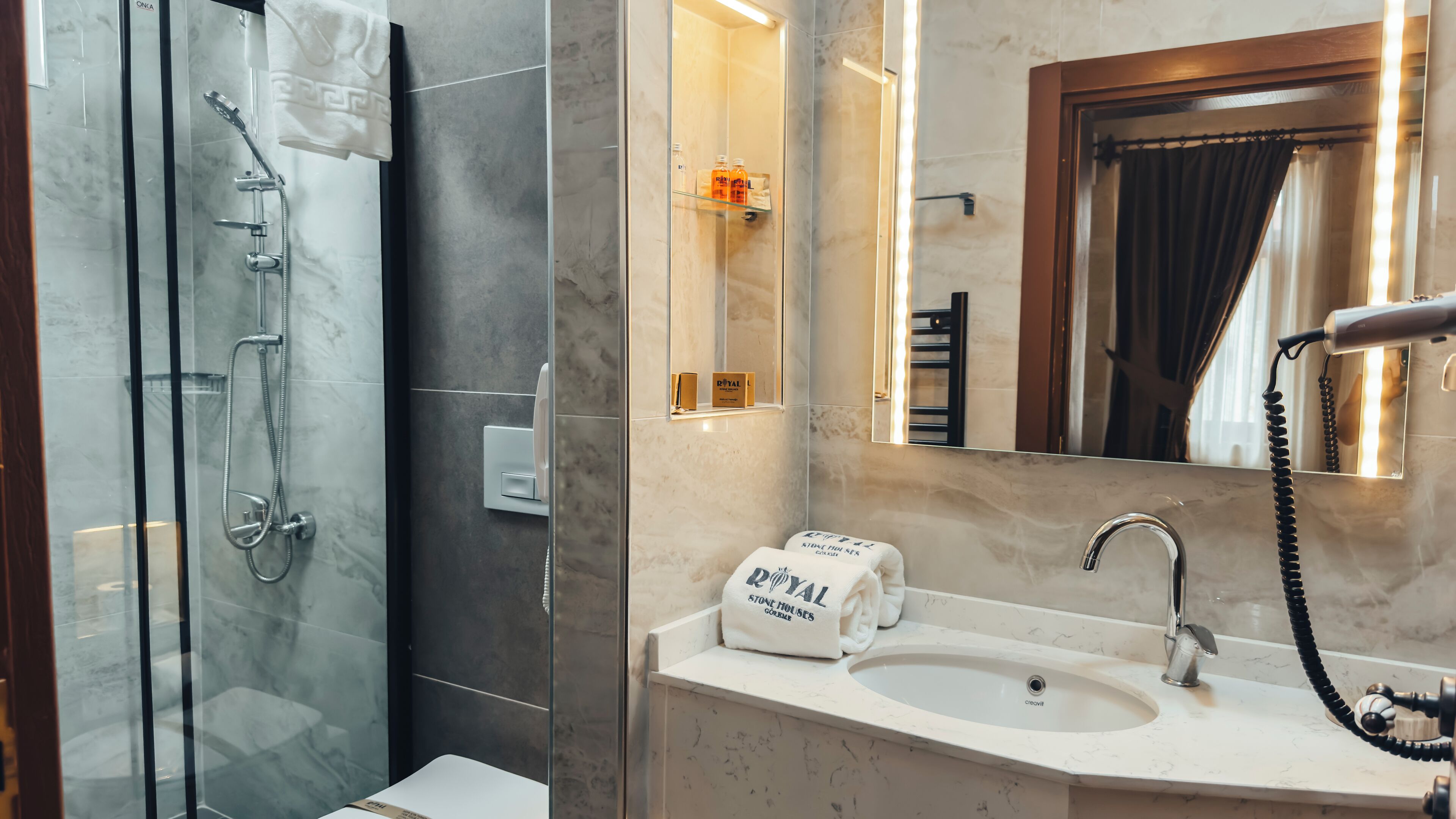 Un baño moderno con ducha envuelta en cristal, lavamanos de mármol y espejo con luz integrada.