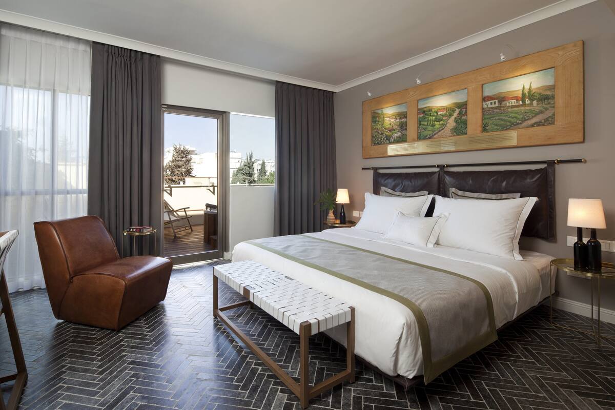 A hotel room with a large bed, a brown leather chair, a small table, and a view of the outdoors.