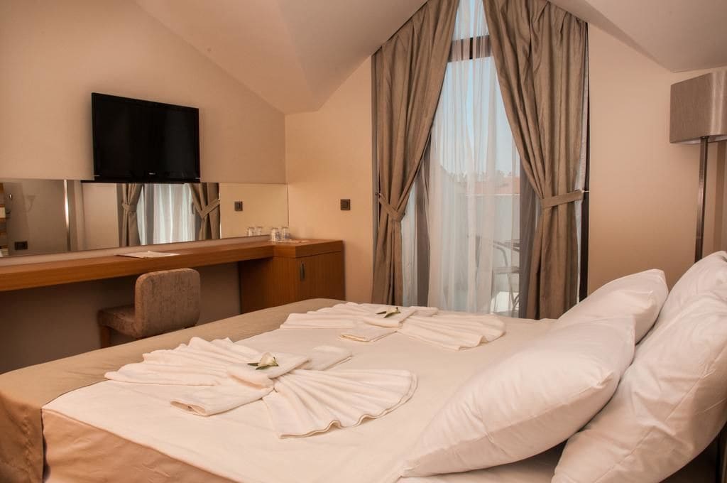 A hotel room with a bed, a desk, a television, and a window with curtains.