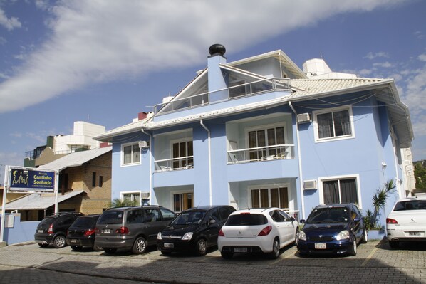 Un immeuble à plusieurs étages avec une façade bleue, plusieurs voitures garées et une enseigne indiquant « Cantinho Sonhado ».