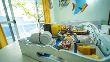 Una bandeja de desayuno con diferentes alimentos y un vaso de jugo de naranja sobre una mesa en una habitación con vistas al exterior.