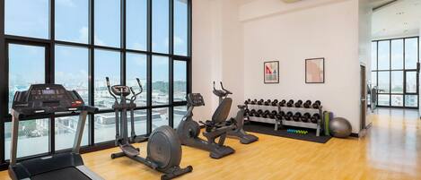 Une salle de sport équipée de tapis de course, de vélos elliptiques et de vélos d’appartement, avec une vue sur la ville grâce à de grandes fenêtres.