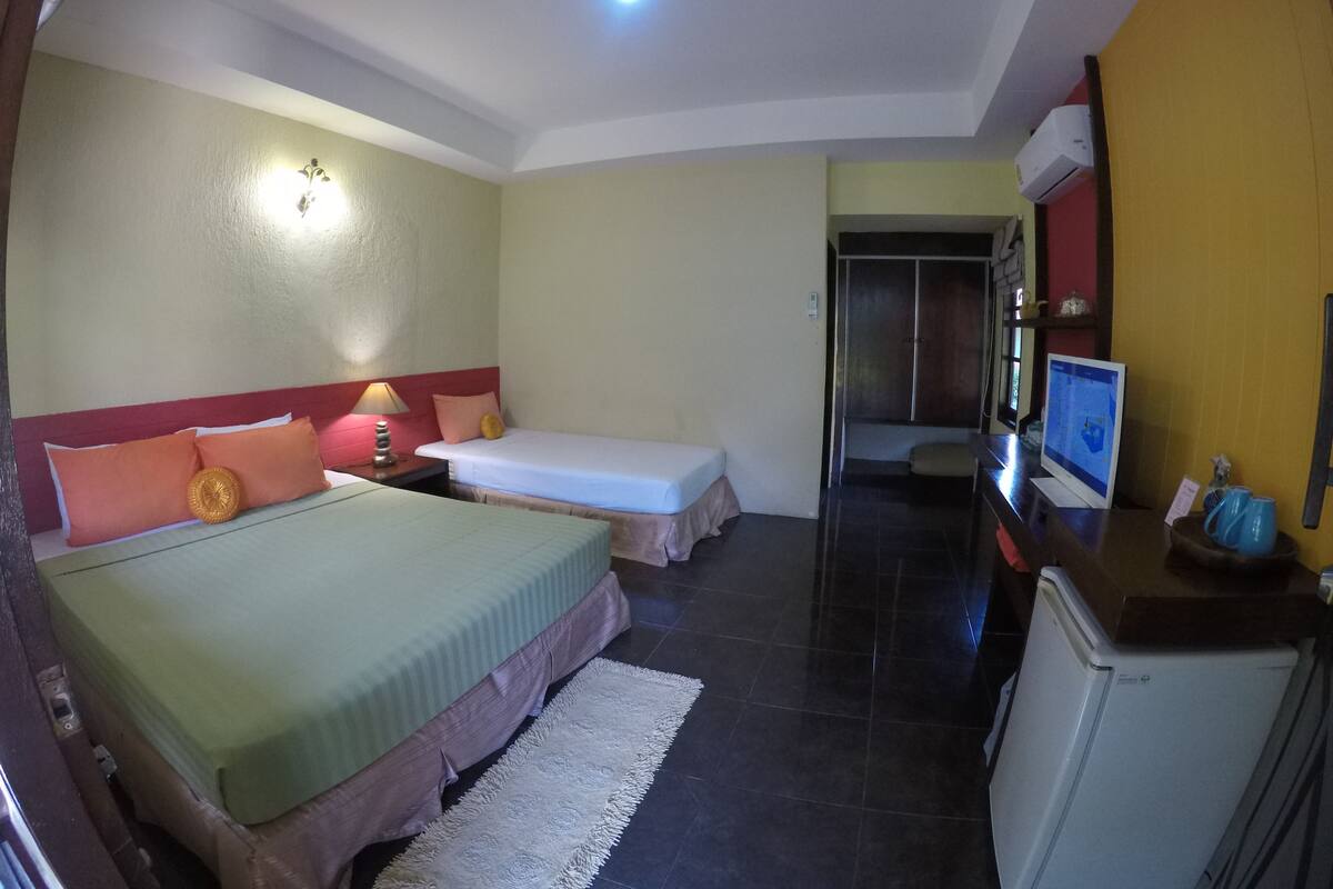 Een hotelkamer met twee bedden, een bureau met een computer, een koelkast en een badkamer die door een geopende deur zichtbaar is.
