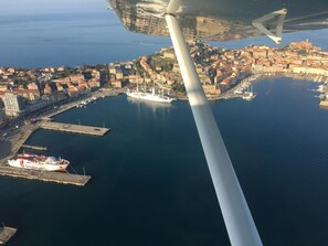An aerial view of a coastal city with a prominent ship docked at a marina, surrounded by buildings and a clear sky. - Agriturismo ORIONE (Campo nell'Elba)