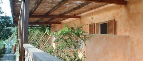 A covered outdoor area with a wooden fence, a pergola, and a building with a peach-colored wall and wooden shutters.