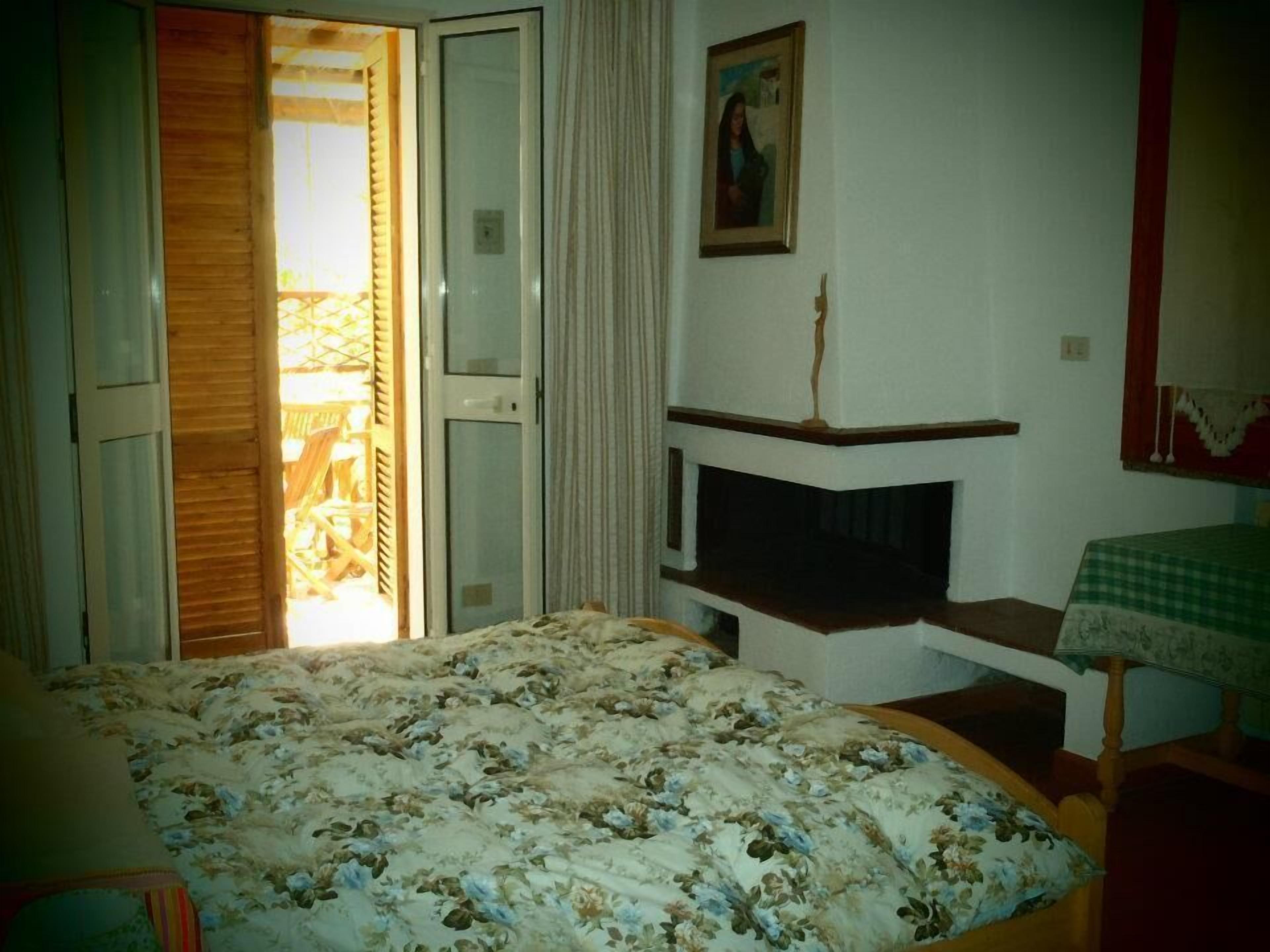 Une chambre à coucher comprenant un lit, une petite table, une chaise, un tableau et une porte donnant sur un espace extérieur.